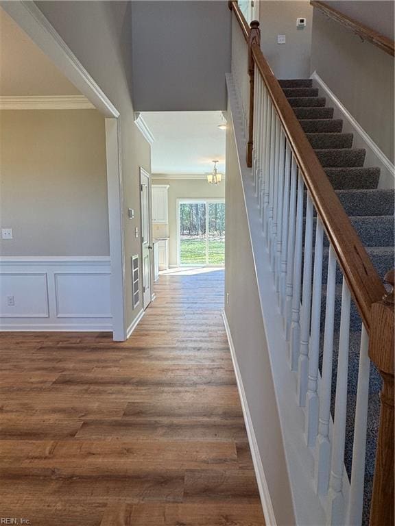 staircase featuring a wainscoted wall, a decorative wall, crown molding, and wood finished floors