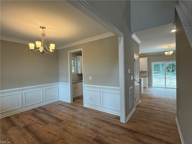 spare room with a chandelier, dark wood-type flooring, wainscoting, and crown molding