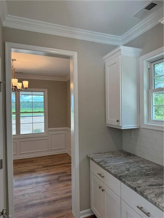 interior space featuring light stone counters, white cabinets, crown molding, and wood finished floors