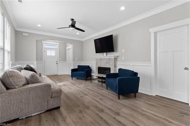 living room with arched walkways, ceiling fan, a tile fireplace, light wood-style flooring, and crown molding