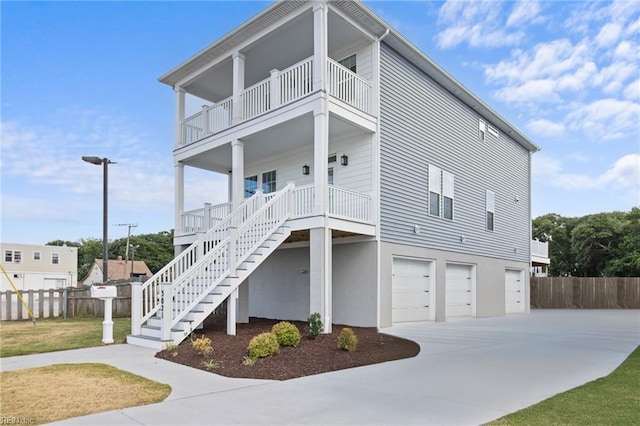 beach home featuring a garage, covered porch, fence, and stairs