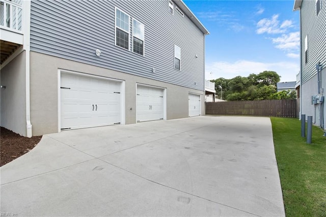 view of home's exterior with a garage, driveway, fence, and stucco siding