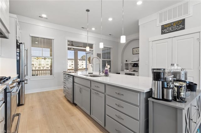 kitchen with a center island with sink, light wood finished floors, gray cabinets, appliances with stainless steel finishes, and a sink