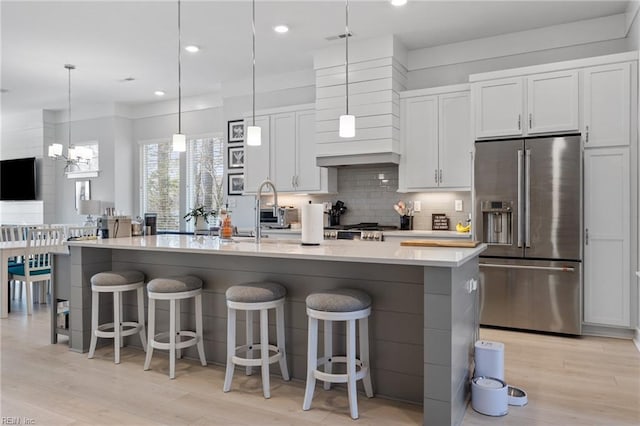 kitchen featuring high end fridge, light wood-style flooring, decorative backsplash, white cabinets, and a kitchen island with sink