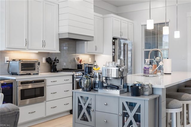 kitchen featuring decorative backsplash, high quality appliances, a breakfast bar area, light countertops, and premium range hood