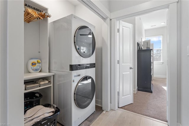 laundry area featuring laundry area, baseboards, stacked washer and clothes dryer, wood finished floors, and carpet