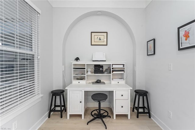 office space with light wood-style floors, arched walkways, and baseboards