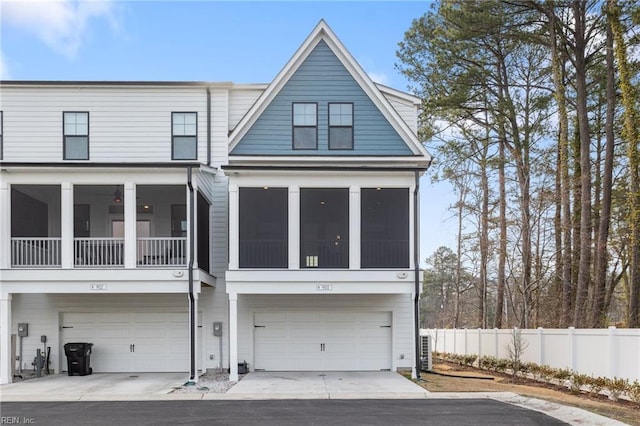 view of front of home featuring a garage, concrete driveway, fence, and a sunroom