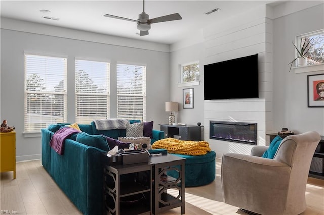 living area featuring light wood-style flooring, visible vents, ceiling fan, and a glass covered fireplace