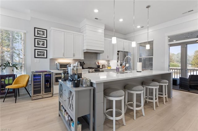 kitchen featuring wine cooler, a sink, light countertops, decorative backsplash, and plenty of natural light