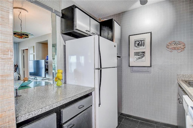 kitchen featuring light countertops, dark tile patterned floors, freestanding refrigerator, and tile walls