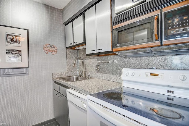 kitchen with white appliances, decorative backsplash, a sink, light countertops, and tile walls