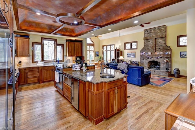 kitchen featuring a center island with sink, a sink, light wood-style floors, light stone countertops, and a brick fireplace