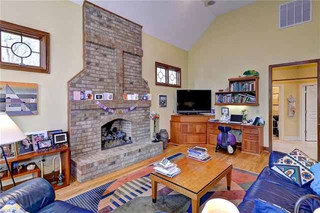 living area with visible vents, a brick fireplace, light wood-type flooring, and vaulted ceiling