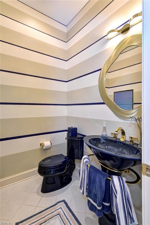 half bath featuring tile patterned floors, toilet, baseboards, and a sink