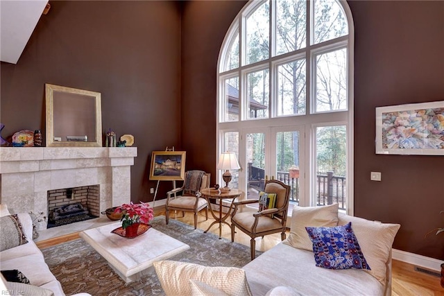 living room with visible vents, a tiled fireplace, wood finished floors, baseboards, and a towering ceiling