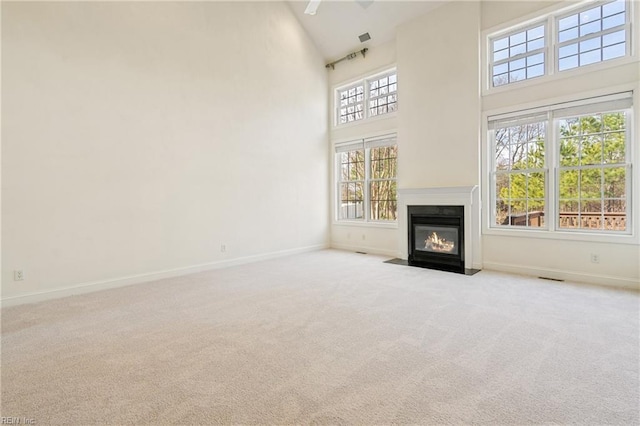 unfurnished living room featuring baseboards, high vaulted ceiling, carpet flooring, and a fireplace with flush hearth