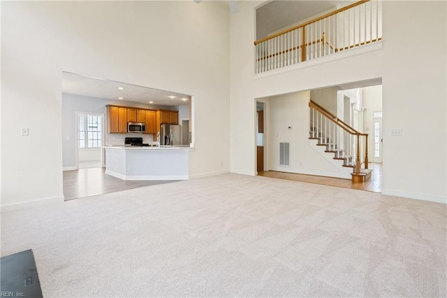 unfurnished living room with visible vents, light colored carpet, stairway, and baseboards