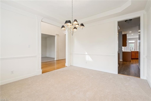 carpeted empty room with baseboards, a notable chandelier, crown molding, and a sink