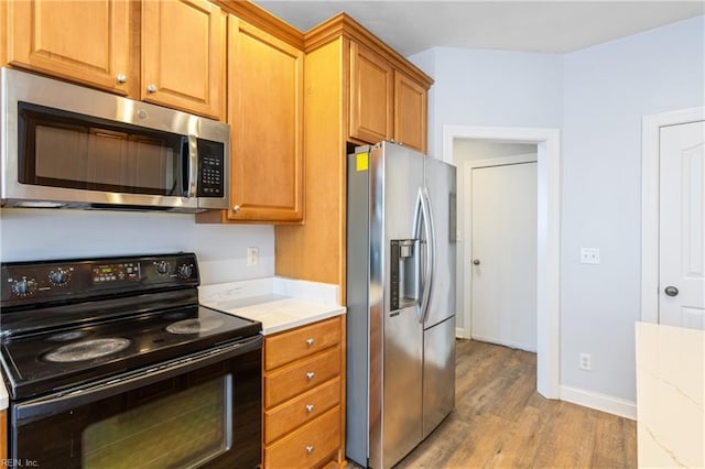 kitchen featuring brown cabinets, appliances with stainless steel finishes, light stone countertops, light wood-type flooring, and baseboards