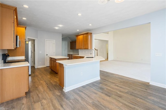 kitchen featuring wood finished floors, a kitchen island, a sink, appliances with stainless steel finishes, and brown cabinetry