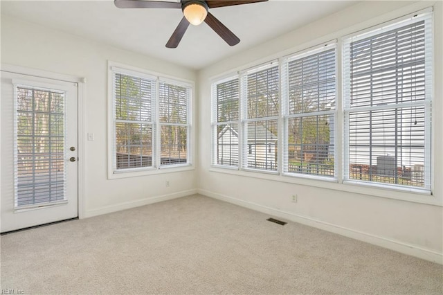 unfurnished sunroom featuring a healthy amount of sunlight, ceiling fan, and visible vents