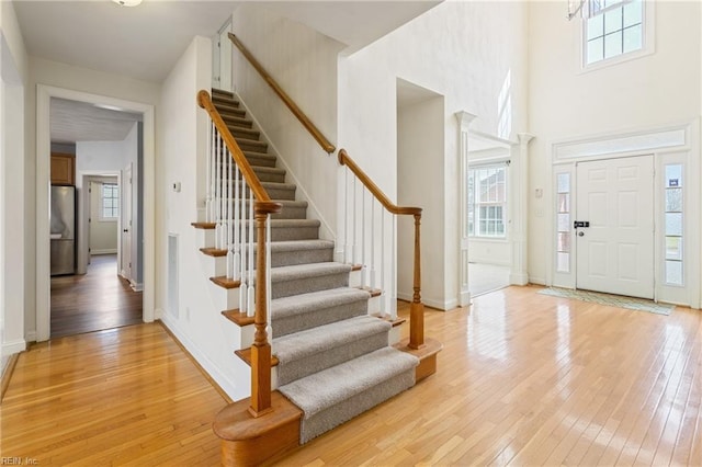 entryway with visible vents, a towering ceiling, baseboards, stairway, and light wood finished floors