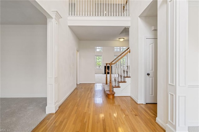 foyer with baseboards, hardwood / wood-style floors, a high ceiling, stairs, and ornate columns