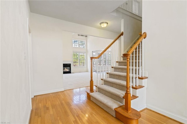 stairway with wood-type flooring, baseboards, and a glass covered fireplace