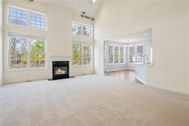 unfurnished living room featuring carpet floors, a high ceiling, a notable chandelier, and a fireplace with flush hearth