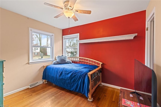 bedroom with a ceiling fan, wood-type flooring, visible vents, and baseboards