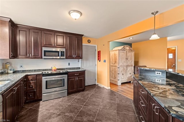 kitchen featuring dark tile patterned flooring, dark brown cabinets, appliances with stainless steel finishes, dark stone countertops, and pendant lighting