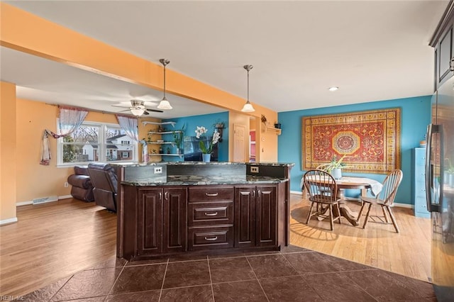 kitchen featuring decorative light fixtures, dark wood-type flooring, open floor plan, dark brown cabinets, and dark stone counters