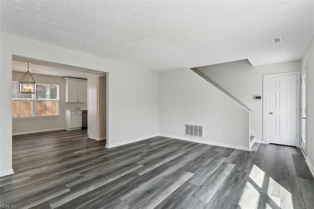 unfurnished living room with dark wood-style floors, stairway, visible vents, and baseboards