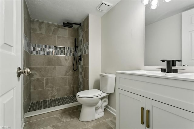 bathroom with toilet, tile patterned flooring, a tile shower, and vanity