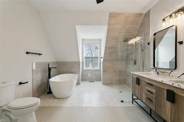 bathroom with double vanity, toilet, walk in shower, a freestanding bath, and tile walls