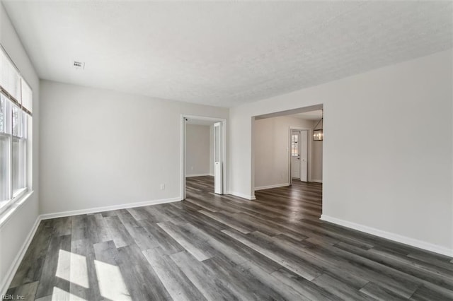 empty room featuring a textured ceiling, baseboards, and dark wood-style flooring