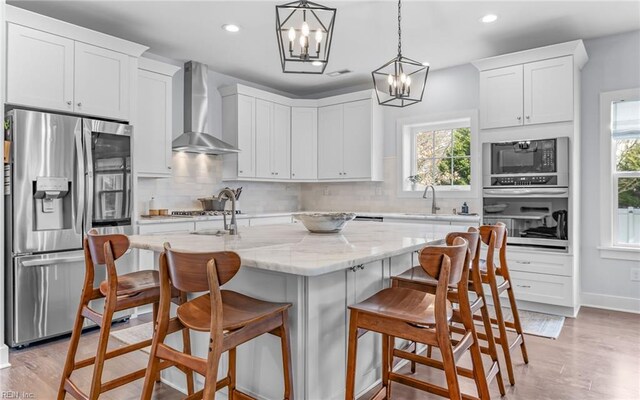 kitchen featuring a sink, backsplash, appliances with stainless steel finishes, white cabinets, and wall chimney range hood