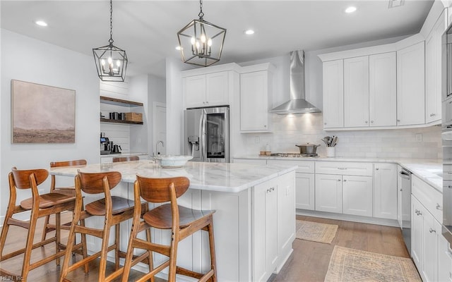 kitchen with light wood-type flooring, white cabinetry, appliances with stainless steel finishes, and wall chimney range hood