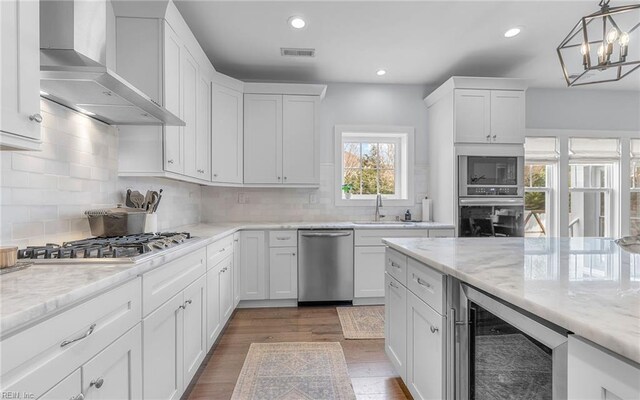 kitchen with wine cooler, white cabinets, stainless steel appliances, wall chimney exhaust hood, and a sink