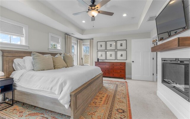 carpeted bedroom with a tray ceiling, multiple windows, a fireplace, and visible vents