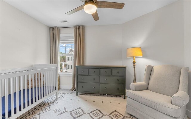 carpeted bedroom featuring visible vents, ceiling fan, and a nursery area