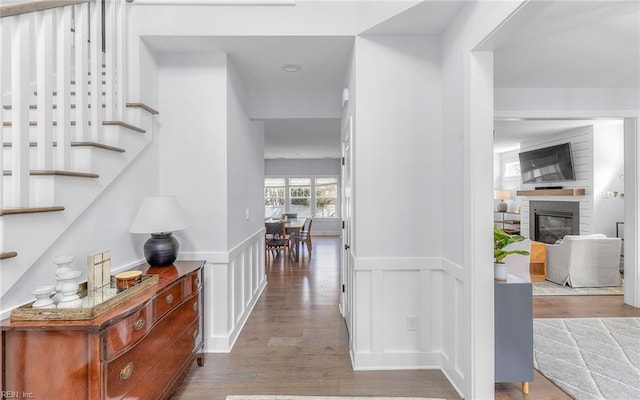 corridor with stairs, a decorative wall, wood finished floors, and a wainscoted wall