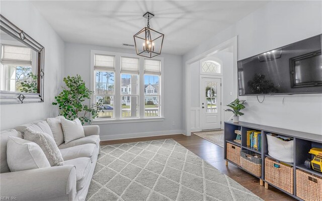 living area featuring a notable chandelier, visible vents, baseboards, and wood finished floors