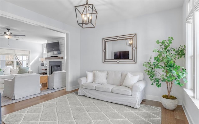 living area with a glass covered fireplace, ceiling fan with notable chandelier, wood finished floors, and baseboards