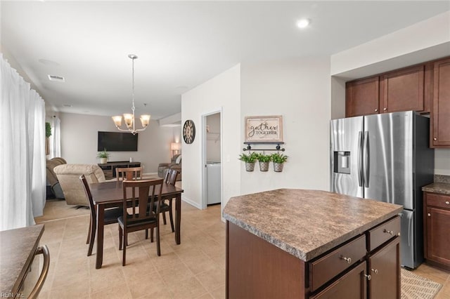 kitchen with stainless steel fridge, visible vents, dark countertops, a kitchen island, and an inviting chandelier