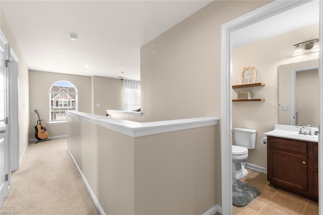 hallway with light colored carpet, baseboards, a sink, and an upstairs landing