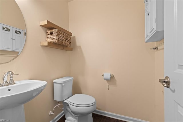 half bathroom featuring toilet, baseboards, a sink, and wood finished floors