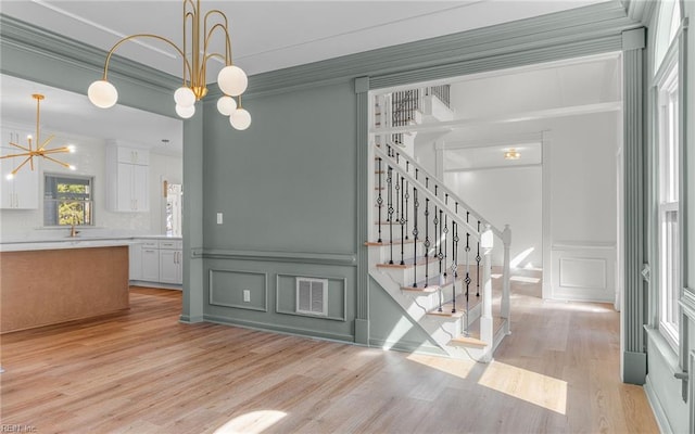 interior space with a wainscoted wall, a notable chandelier, a decorative wall, ornamental molding, and wood finished floors