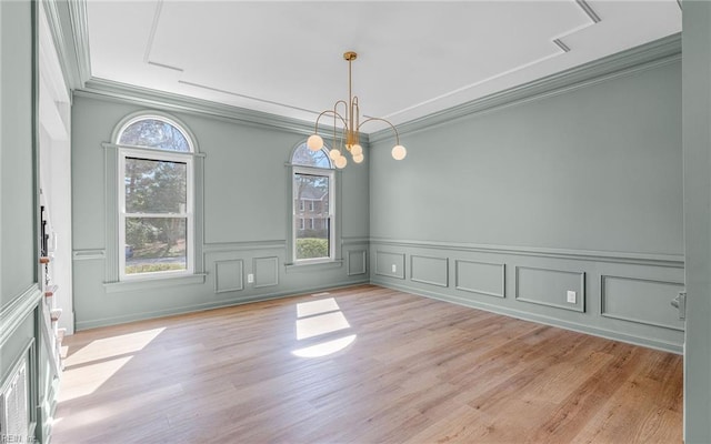 unfurnished dining area with an inviting chandelier, plenty of natural light, ornamental molding, and light wood-style floors